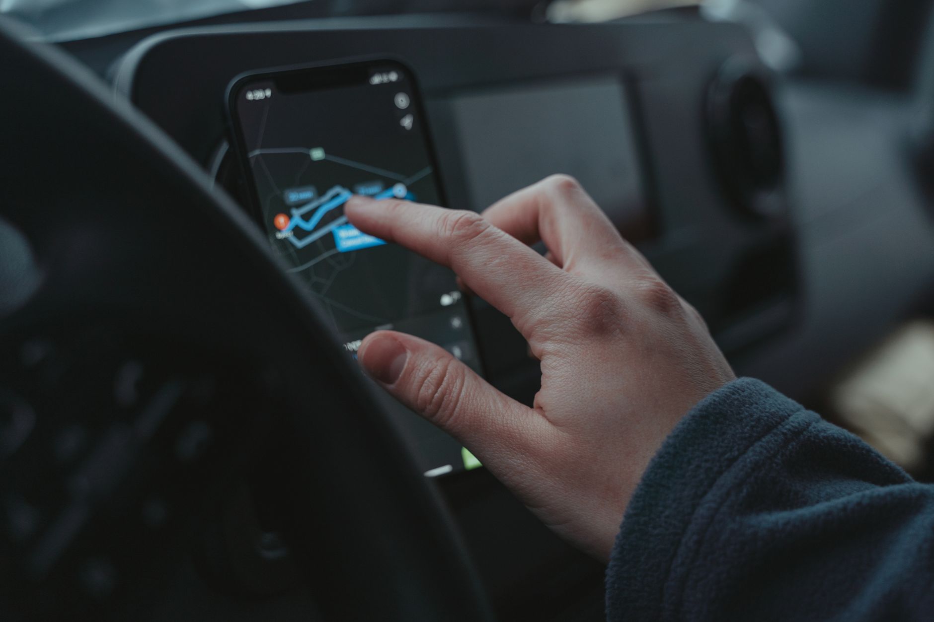 Dłoń ustawiająca na smartfonie nawigację GPS w samochodzie